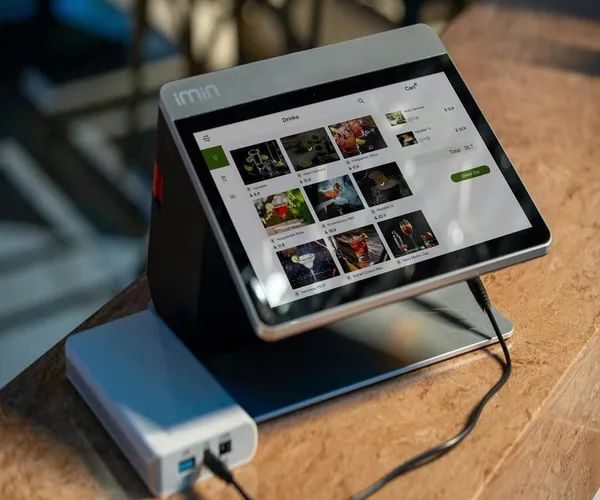 Terminal TPV táctil con menú de bebidas en pantalla, sobre mostrador de mármol